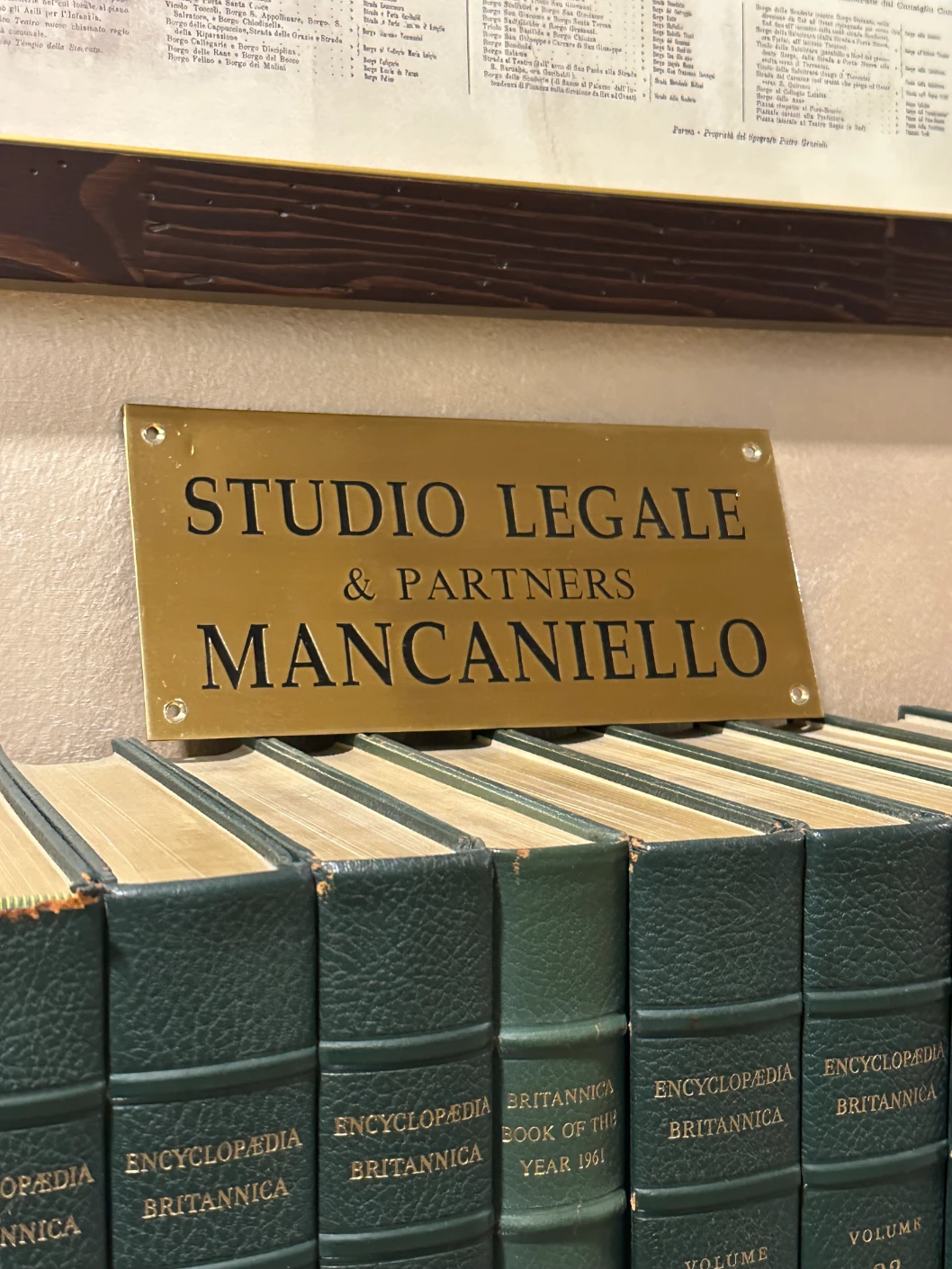 Targa dello Studio Legale Mancaniello & Partners su sfondo di codici giuridici in biblioteca